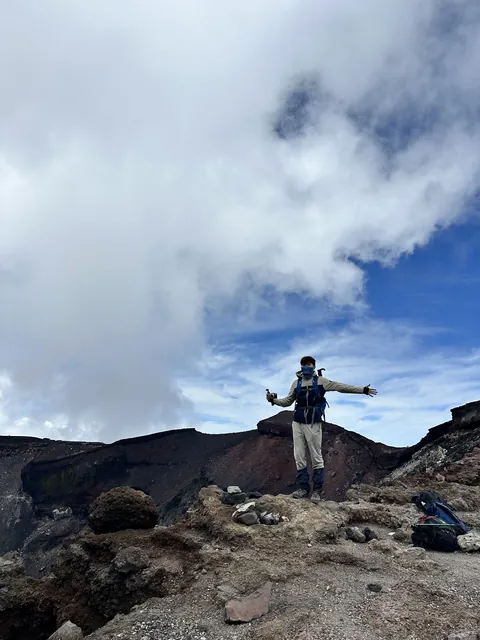 Zuchen with arms spread on the rim of Mount Fuji's summit crater, July 2025